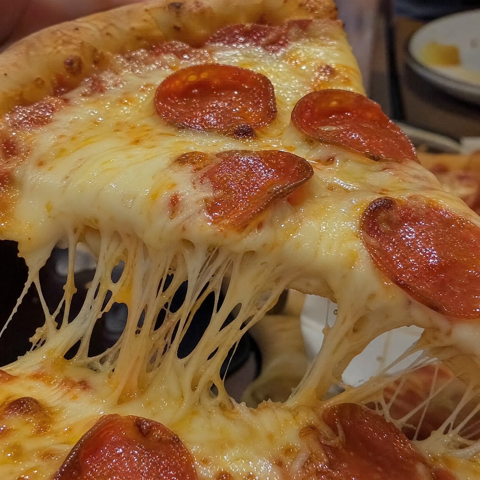 Close-up of a cheesy pepperoni pizza slice being pulled away with melted cheese stretching